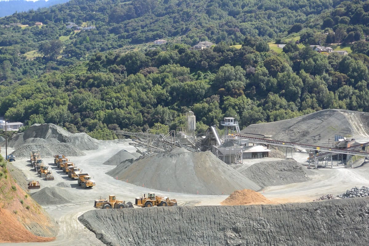 A view of a mountain from above shows many large piles of gravel.