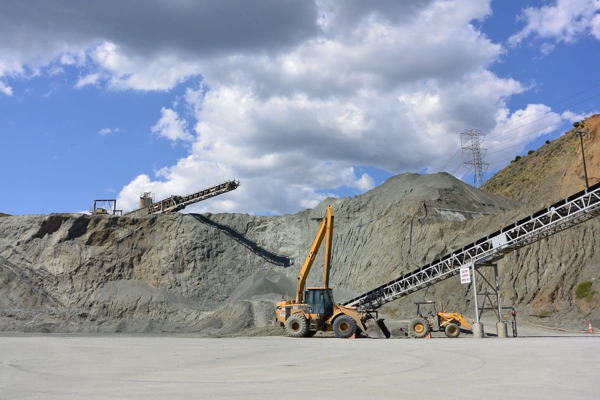A large pile of gravel with two cranes in the background.
